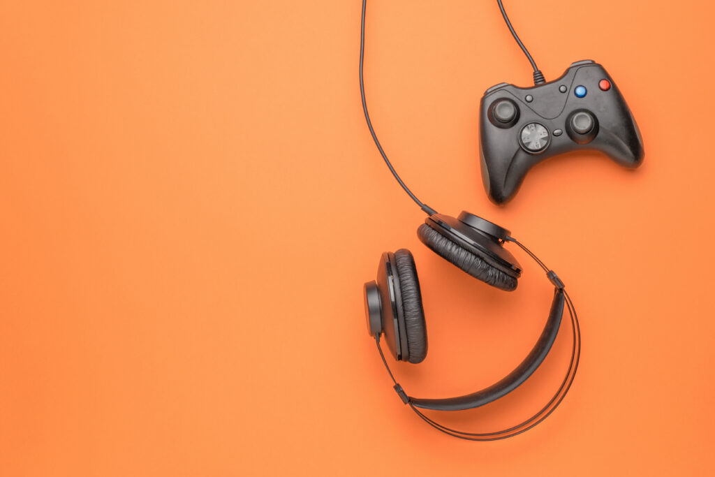 Black headphones and a black game console on an orange background. Flat lay. Place for text.