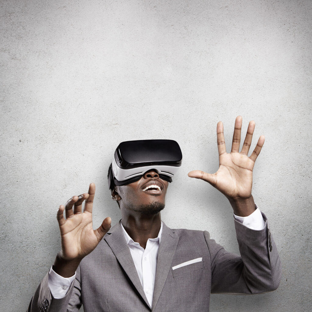 Handsome African entrepreneur dressed in gray suit gesturing and holding his hands as if interacting with something while playing video games using 3d virtual reality headset or oculus glasses